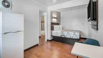 A compact hotel room with a bed, a small table, a chair, a TV mounted on the wall, and a ceiling fan.