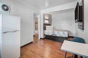 A compact hotel room with a bed, a small table, a chair, a TV mounted on the wall, and a ceiling fan.