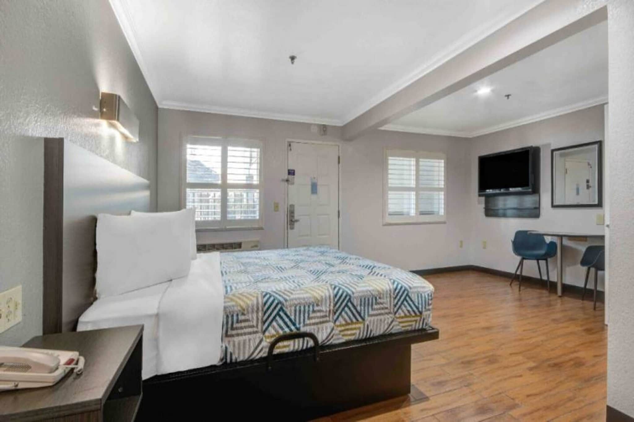 A hotel room with a bed, a desk with a telephone, a TV, and a chair.