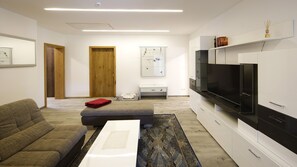 Ein stilvolles Wohnzimmer mit einer Couch, Hocker, Couchtisch und einem Flachbildfernseher.