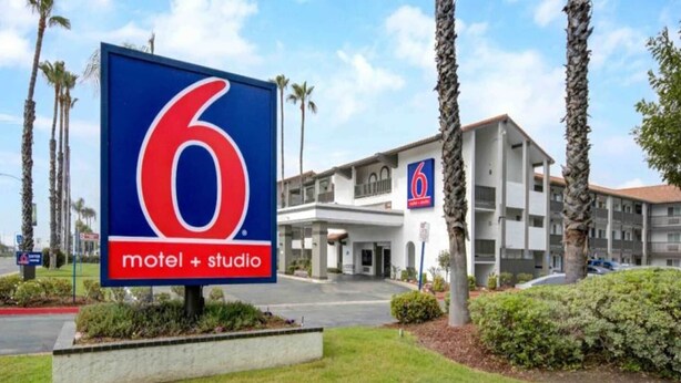 Een motel met een opvallend bord met het cijfer '6', een gebouw met twee verdiepingen en een parkeerplaats.