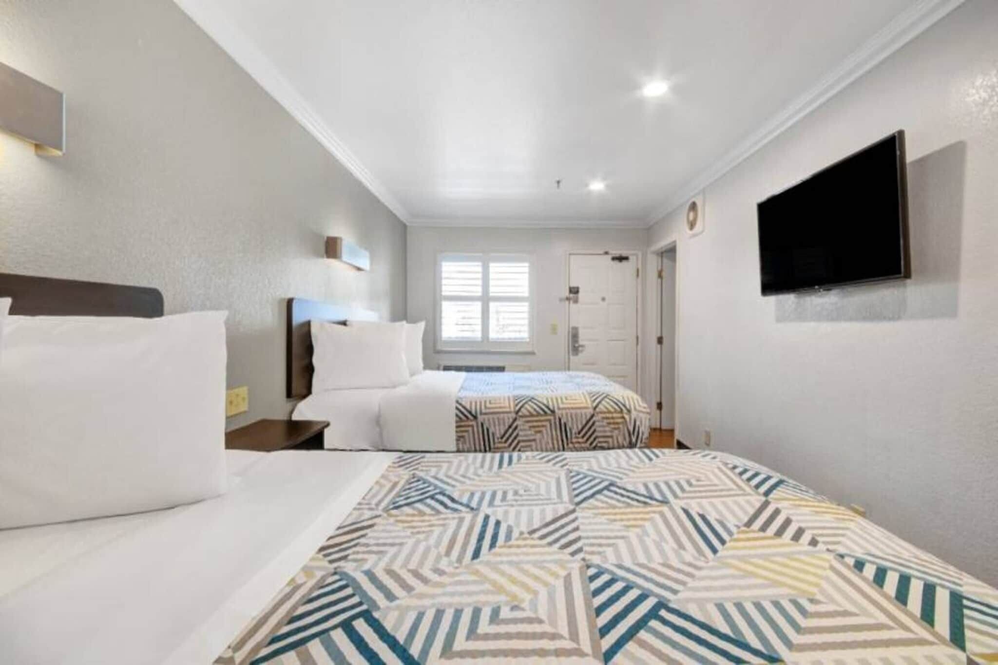 Habitación de hotel con dos camas, un televisor montado en la pared y una ventana con persianas.