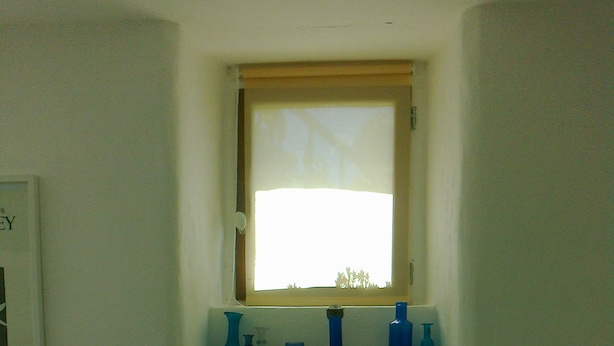 Una ventana pequeña con vistas a árboles, un estante con diversos objetos y una pequeña planta.