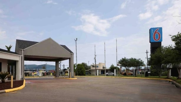 Um estacionamento com área coberta, um edifício com a placa '6' e céu claro.