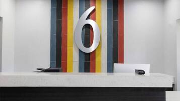 Una mesa de recepción con un gran número '6' en la pared, un teléfono y una pequeña caja, posiblemente una caja registradora.