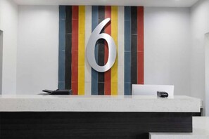 A reception desk with a large number '6' on the wall, a phone, and a small box, possibly a cash register.
