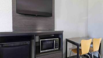 A modern room with a flat-screen TV mounted on the wall, a microwave, a small table, and two chairs.