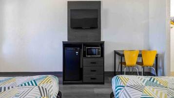 Ein Hotelzimmer mit zwei Betten, einem Schreibtisch, einer Mikrowelle, einem Fernseher und zwei gelben Stühlen.