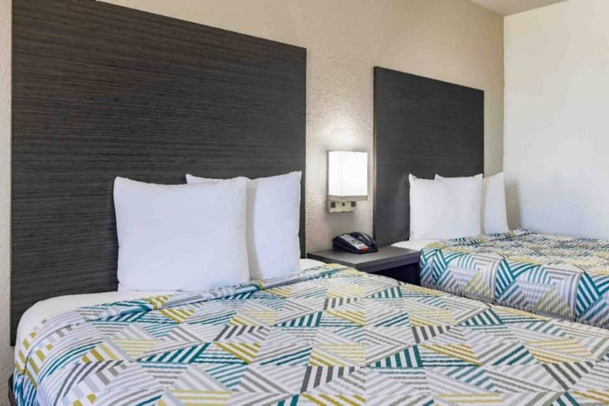 Una habitación de hotel con dos camas, una mesita de noche, un espejo y un teléfono instalado en la pared.