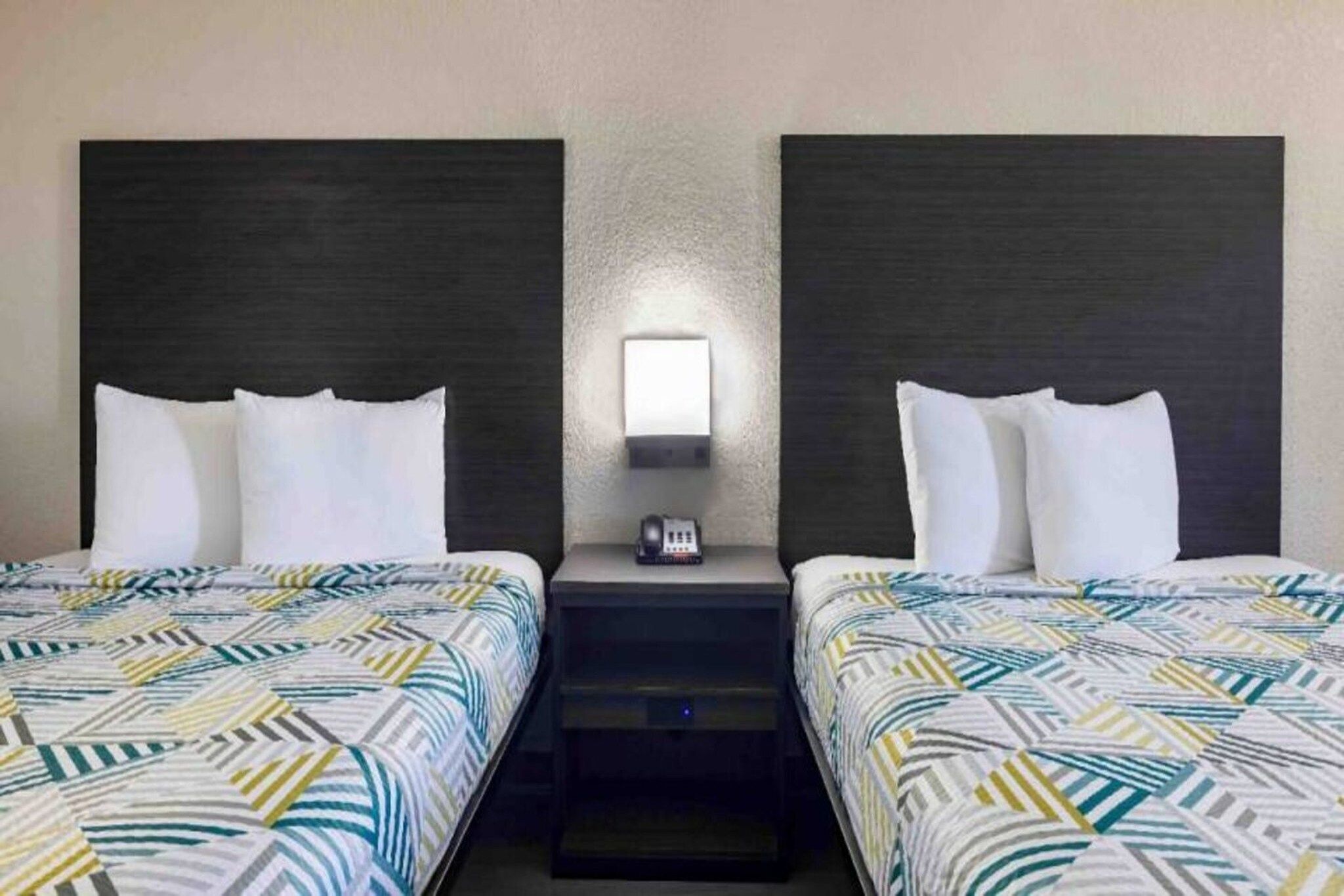 A hotel room with two beds, a nightstand with a phone, and a wall-mounted light.