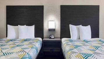 A hotel room with two beds, a nightstand with a phone, and a wall-mounted light.