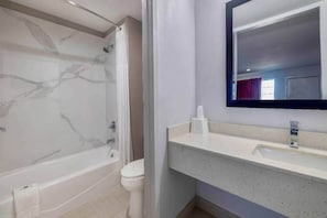 A bathroom with a marble bathtub, a toilet, and a sink with a mirror above it. - Modern 1 King Bed | Non-Smoking (Lake-Charles)