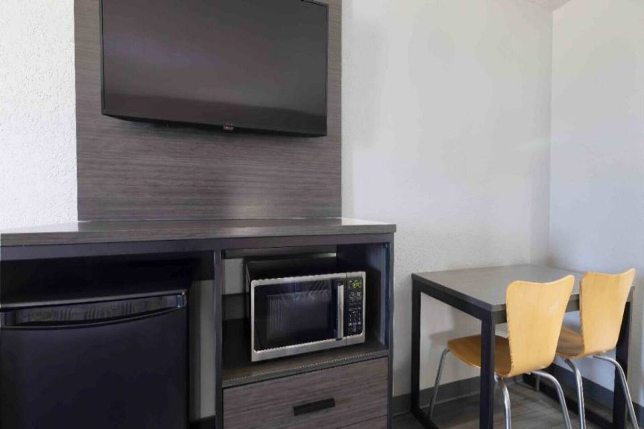 A compact kitchenette with a microwave, a small refrigerator, and a flat-screen TV mounted on the wall.