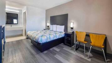 Una habitación de hotel con cama, mesita de noche, dos sillas y televisor montado en la pared.