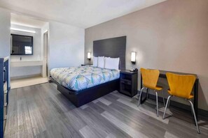 A hotel room with a bed, bedside table, two chairs, and a TV mounted on the wall.