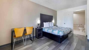 Habitación de hotel con cama, dos sillas, una mesita de noche y un baño visible a través de una puerta abierta.