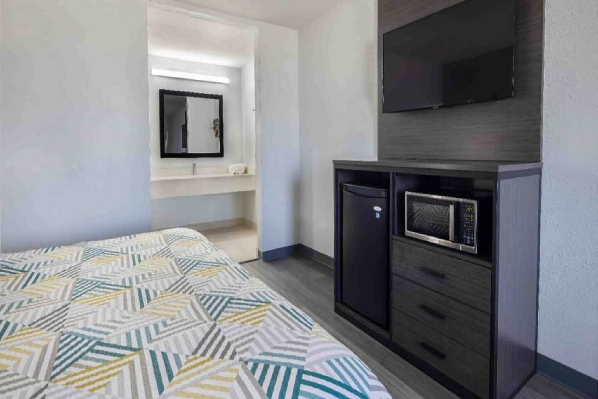 A hotel room with a bed, a television, a microwave, and a small cabinet.