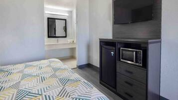 A hotel room with a bed, a television, a microwave, and a small cabinet.
