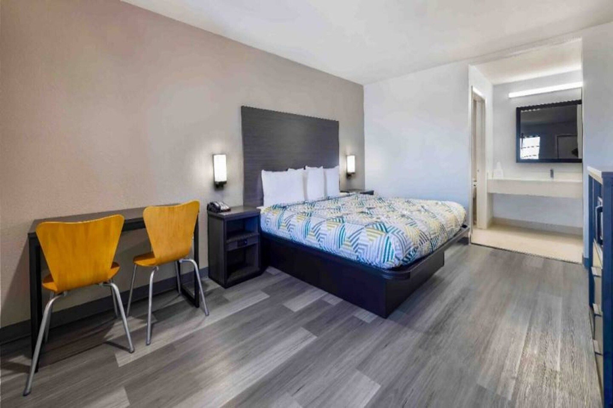 A hotel room with a bed, two chairs, a nightstand, and a TV.