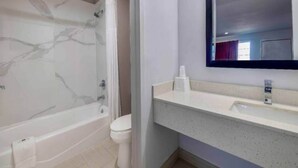 A bathroom with a marble bathtub, a toilet, and a sink with a mirror above it. - 1 King Bed | Mobility Accessible Tub, Nsmk (Lake-Charles)
