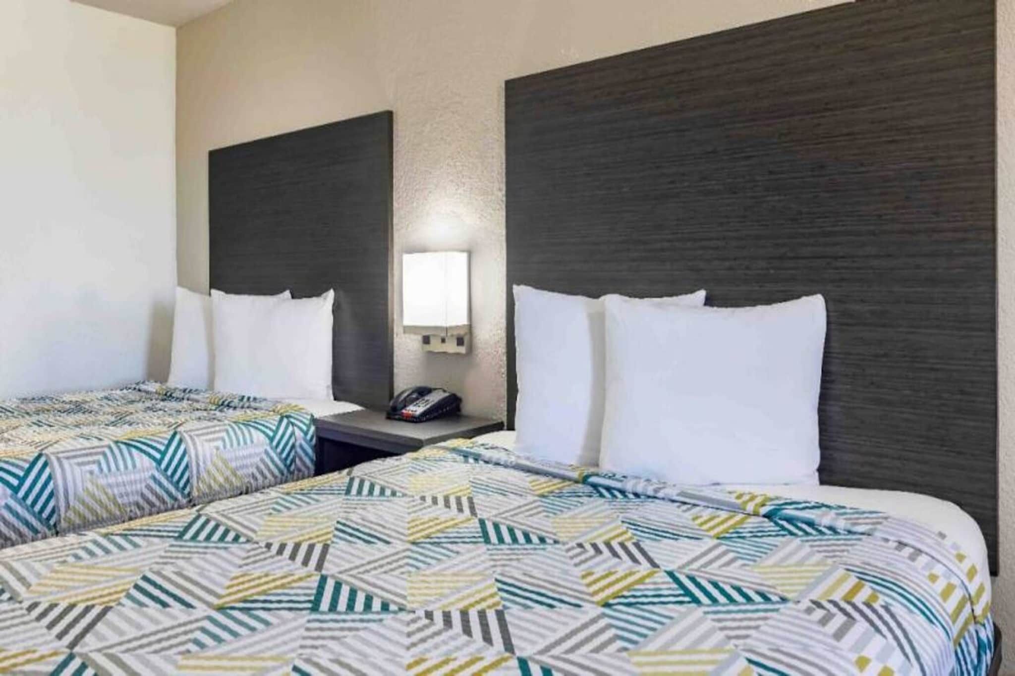 Habitación de hotel con dos camas, cada una con una colcha estampada, una mesita de noche con teléfono y una lámpara fijada a la pared.