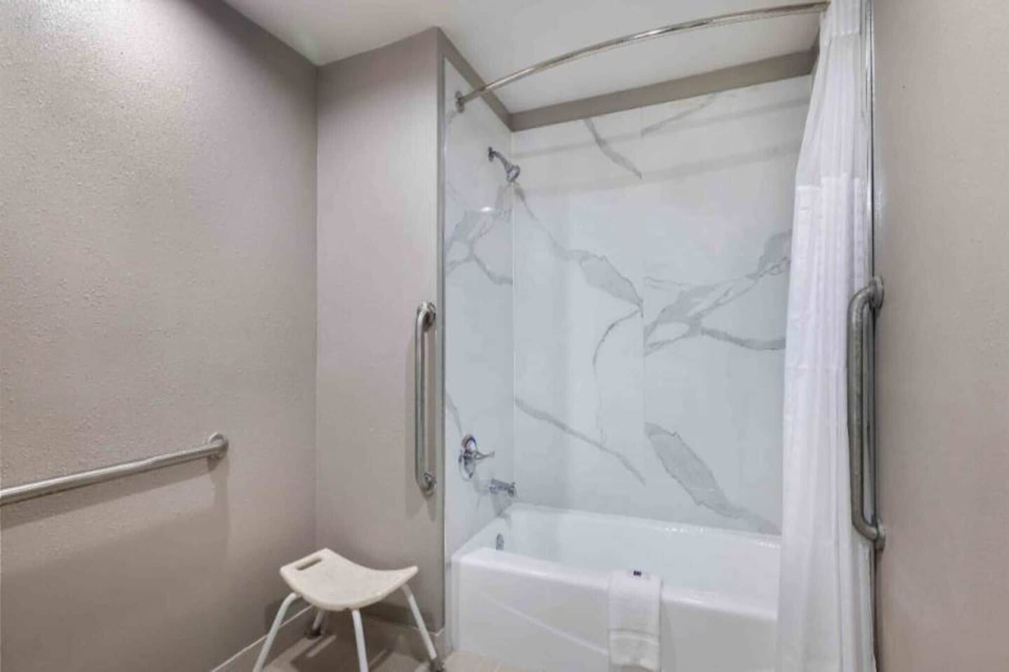 Un baño con cabina de ducha de vidrio, una bañera blanca y un taburete pequeño.