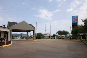 A parking lot with a covered area, a building with a '6' sign, and a clear sky. - Spacious 2 Queen Beds | Non-Smoking (Lake-Charles)