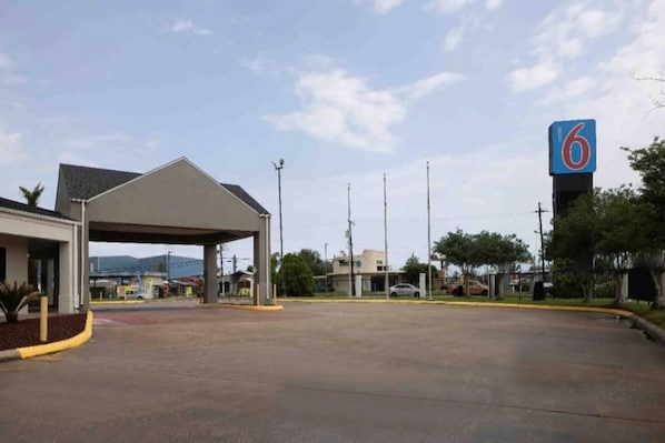 A parking lot with a covered area, a building with a '6' sign, and a clear sky. - Spacious 2 Queen Beds | Non-Smoking (Lake-Charles)