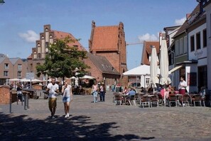 A cobblestone street with outdoor seating, historic buildings, and a church in the background. - Vrbo Property (Wismar)