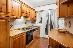 A kitchen with wooden cabinets, a stove, and a sink. - Spacious Apartment for 6 with Tofane Views and Panoramic Terrace (Cortina d'Ampezzo)