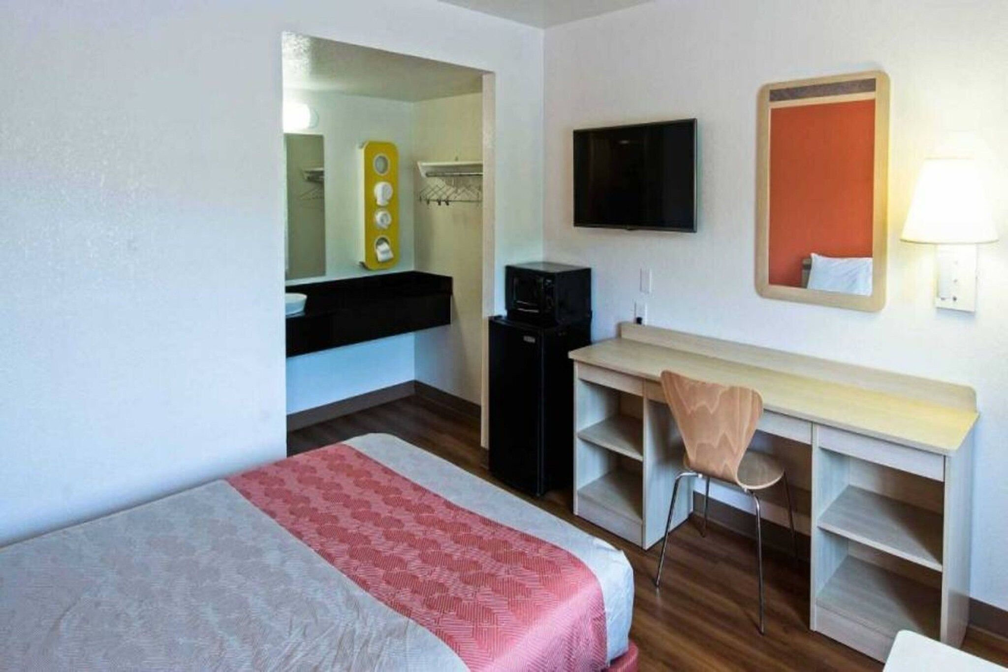 A hotel room with a bed, a desk, a chair, a television, and a mirror.