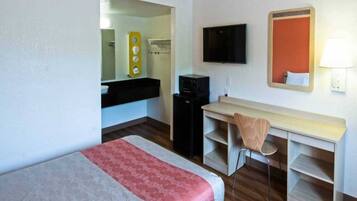 A hotel room with a bed, a desk, a chair, a television, and a mirror.