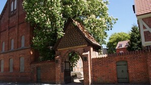 En historisk murstensbygning med et stort træ foran, en port og en brostensbelagt gade.