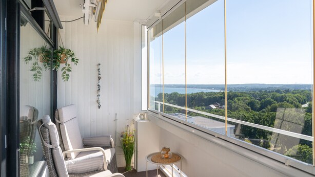 Un balcone con mobili in vimini, un tavolino e vista su un lago e una foresta.