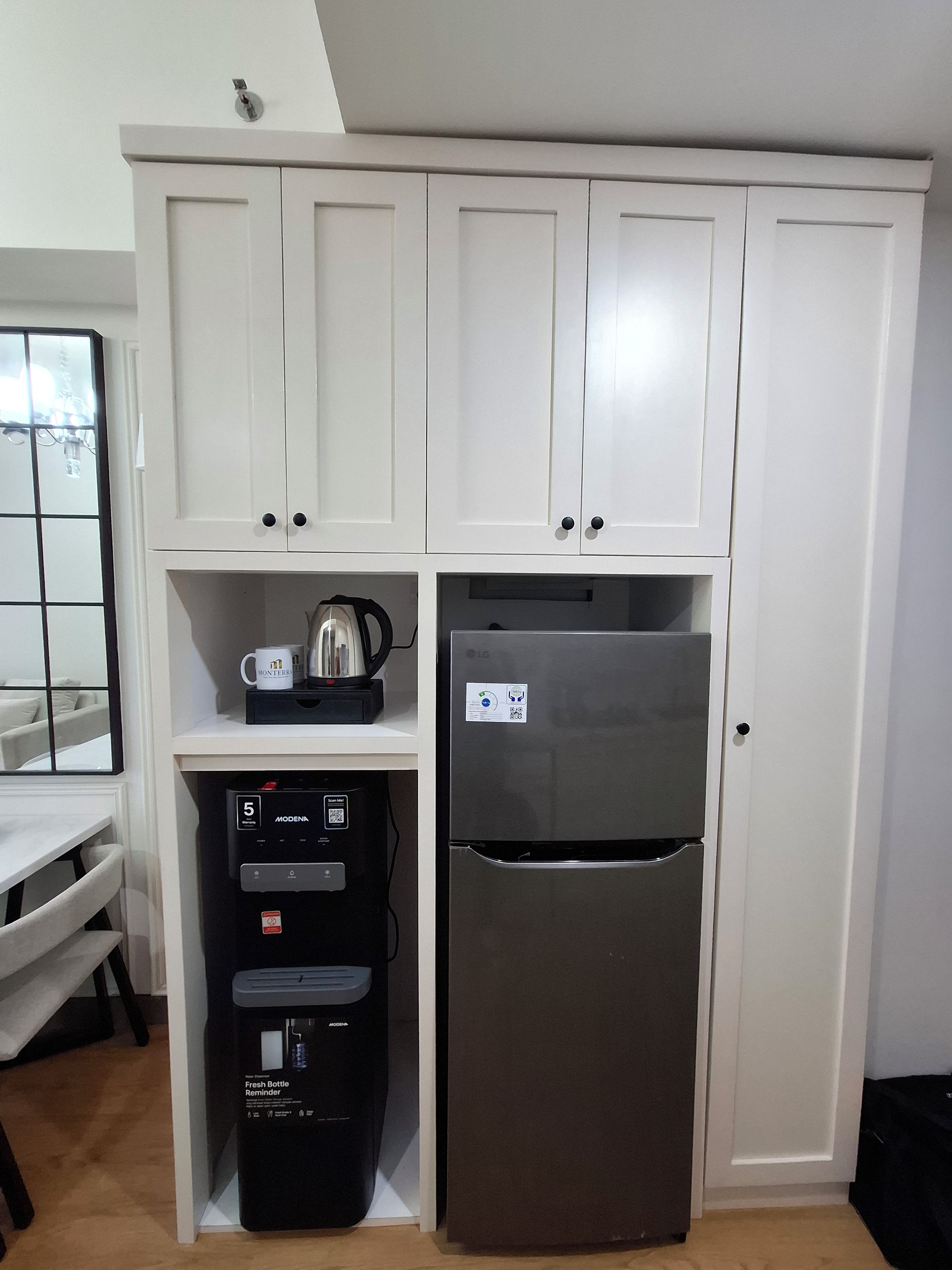 A kitchenette with white cabinets, a stainless steel refrigerator, a coffee maker, and a water dispenser.