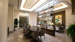 A modern dining area with a long table, chairs, and a decorative bookshelf. - Apartement Pakuwon Bekasi by Monterra (Jawa Barat)