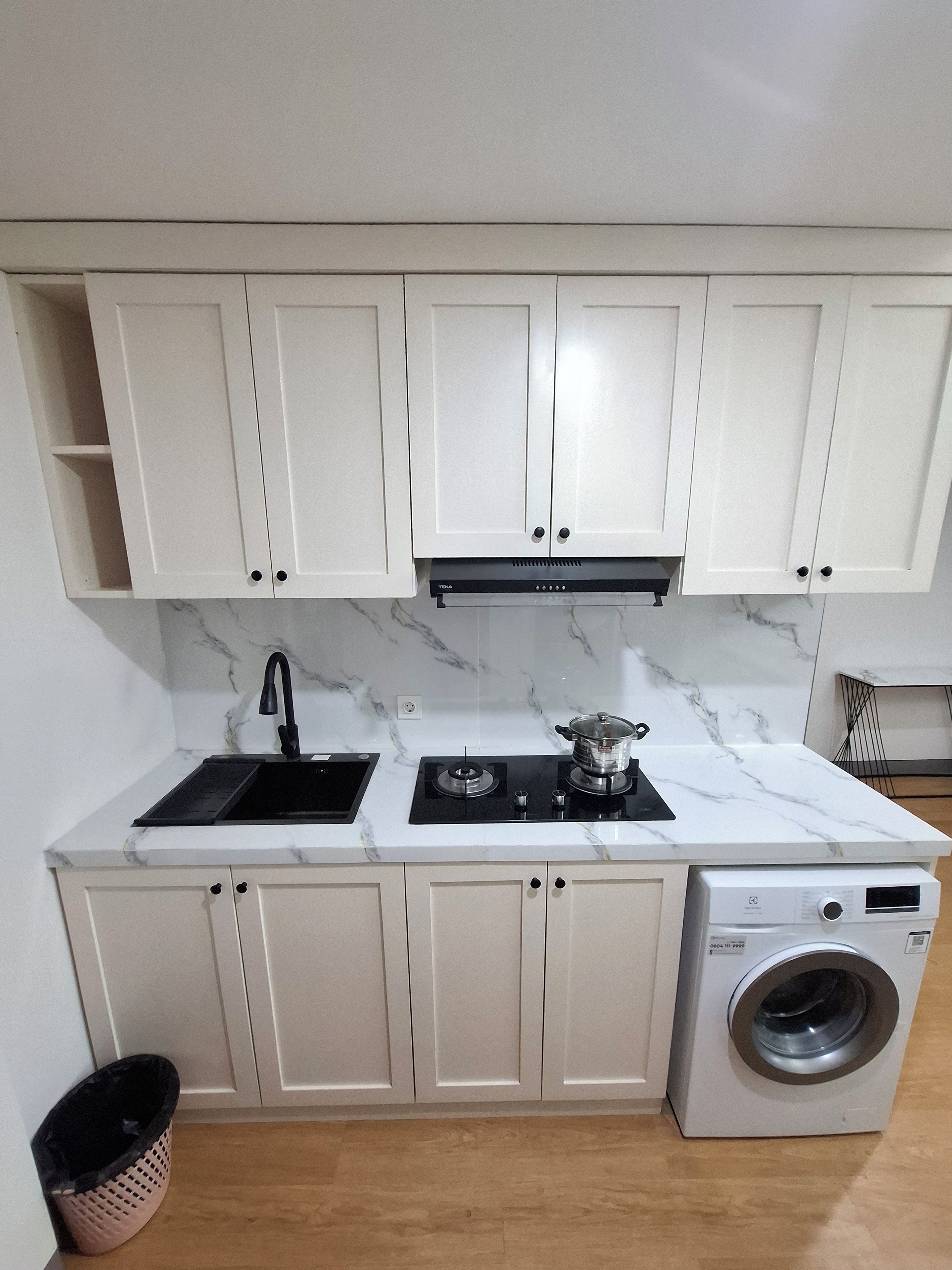 Una cocina con armarios blancos, un lavabo negro, una estufa y una lavadora integrada.