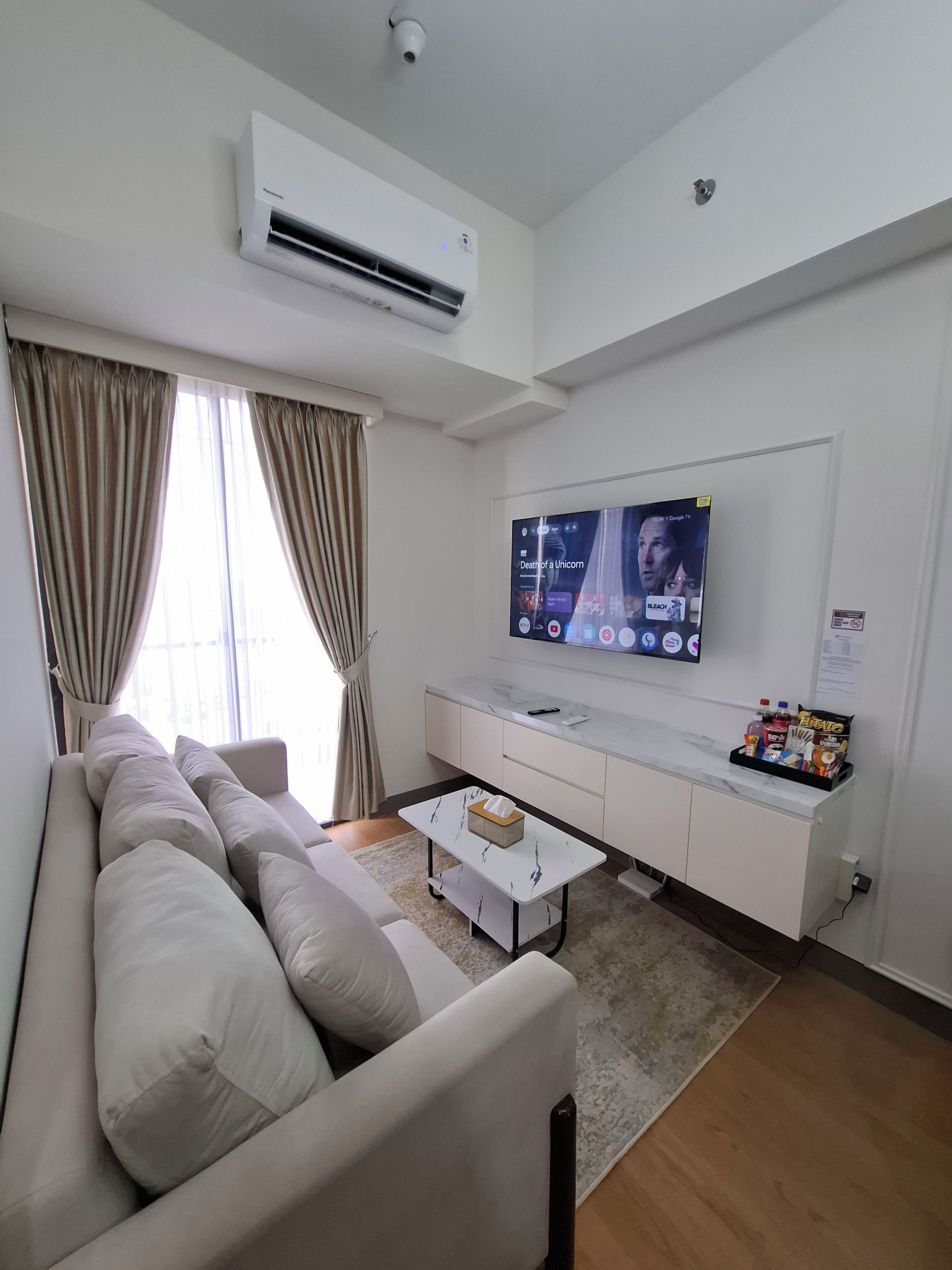 A modern living room with a sofa, a coffee table, a flat-screen TV, and an air conditioning unit.