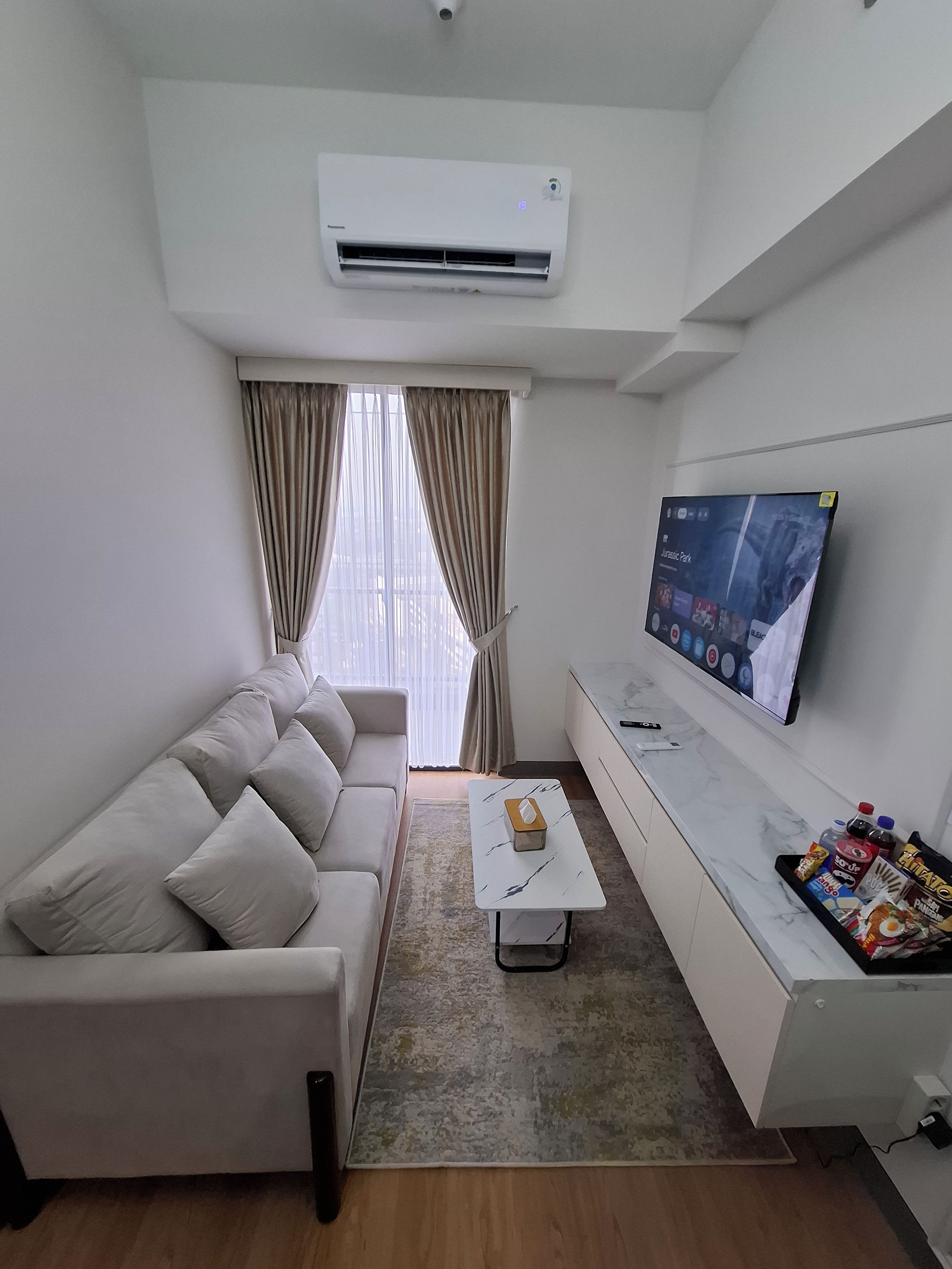 Una sala de estar moderna con sofá, una mesa de centro, un televisor de pantalla plana montado en la pared y un equipo de aire acondicionado.
