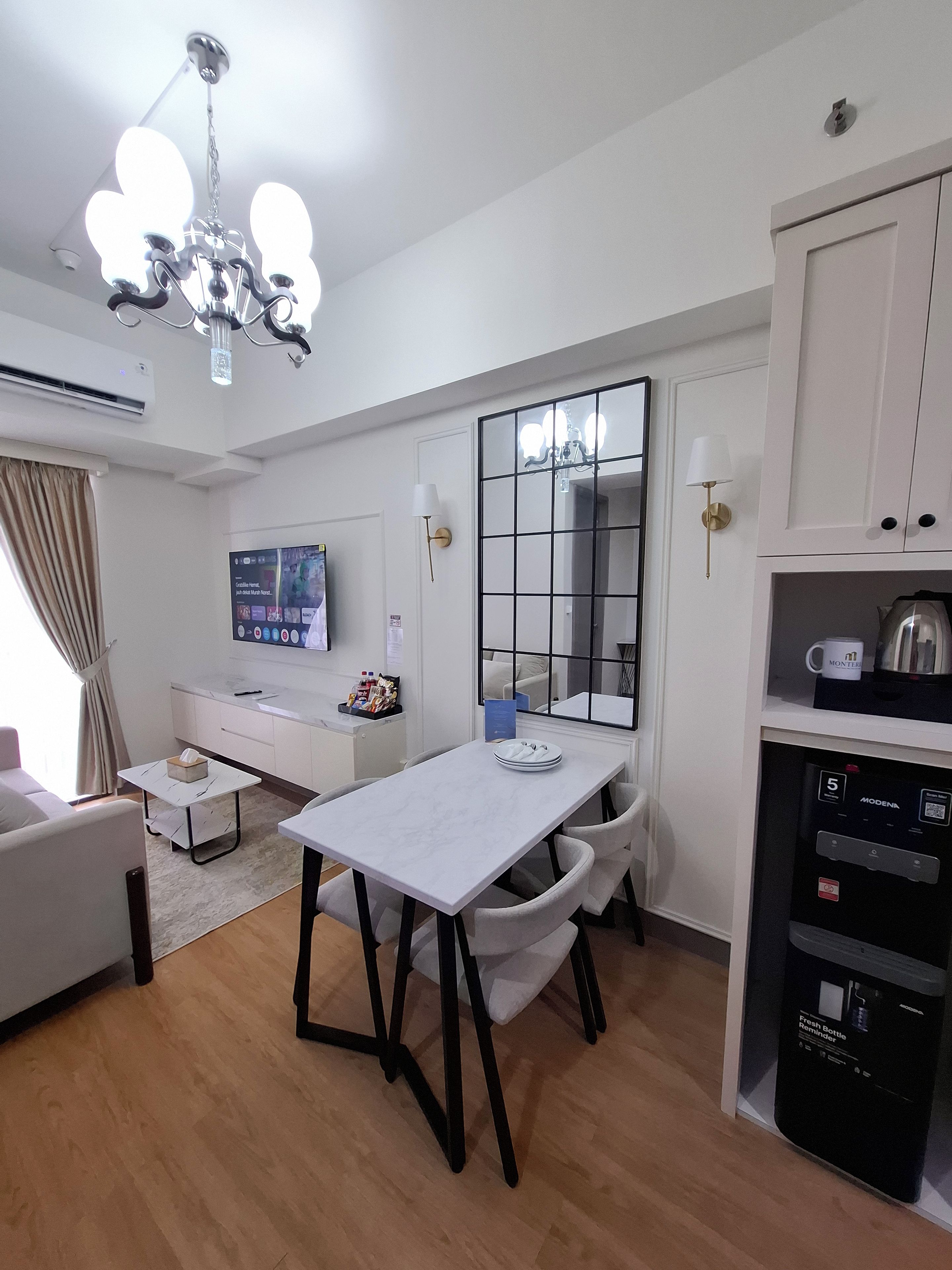 Una sala de estar moderna con comedor, televisión, cafetera y un ventanal grande.
