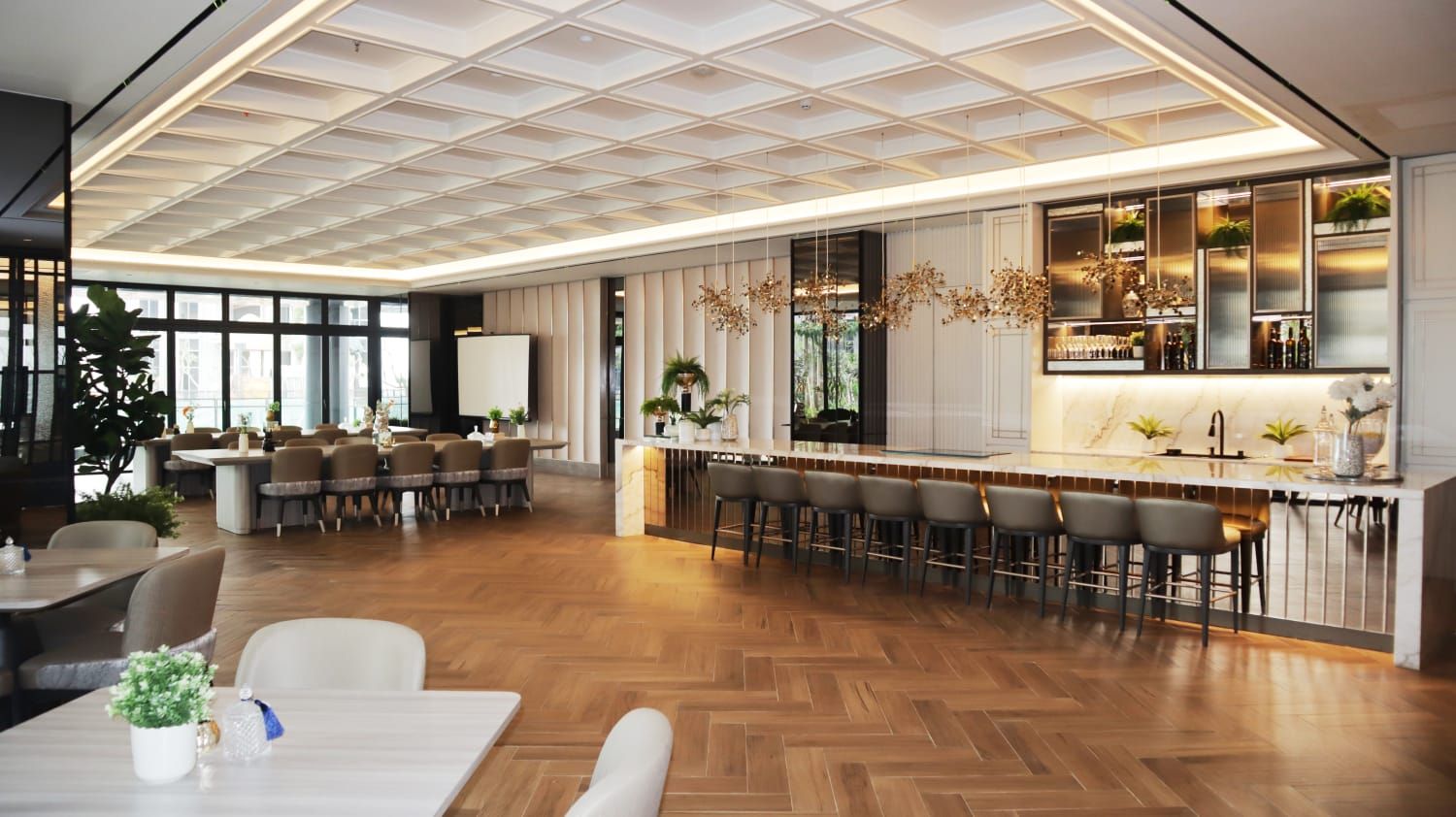 Un interior moderno con suelo de madera en espiga, una zona de bar con taburetes y un área de estar con mesas y sillas.