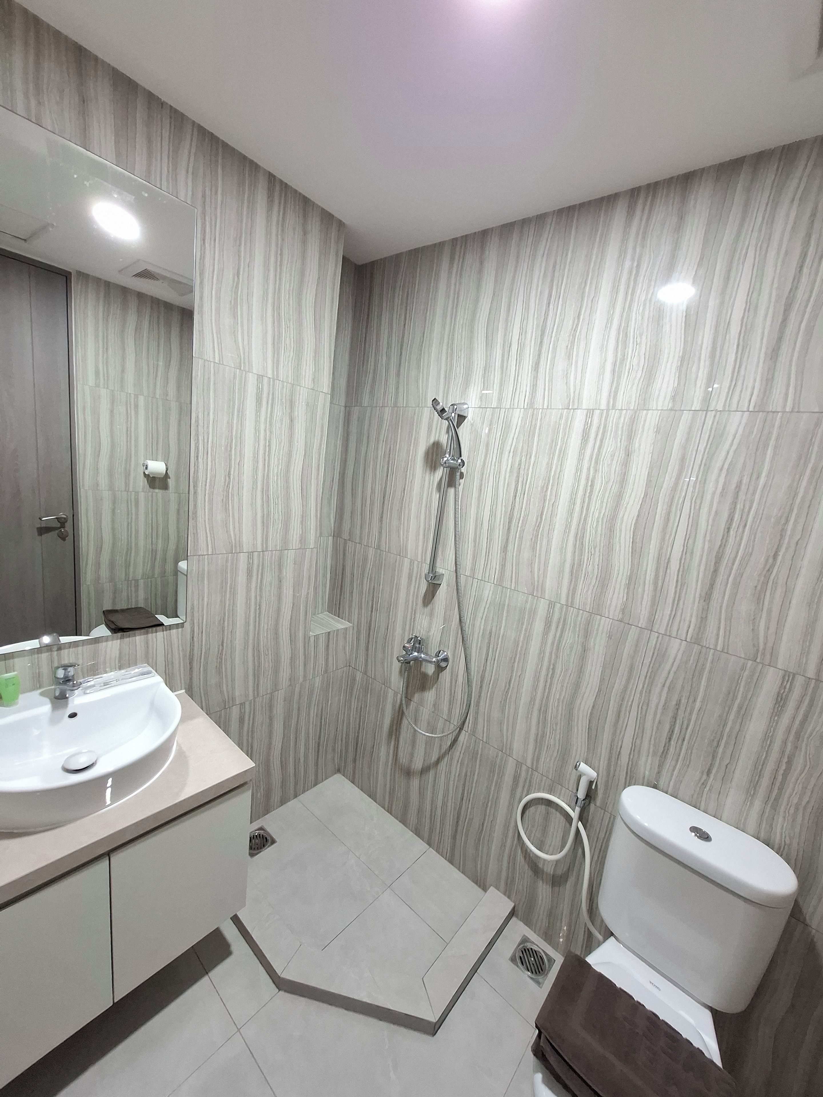 A bathroom with a sink, mirror, shower, toilet, and a towel rack.