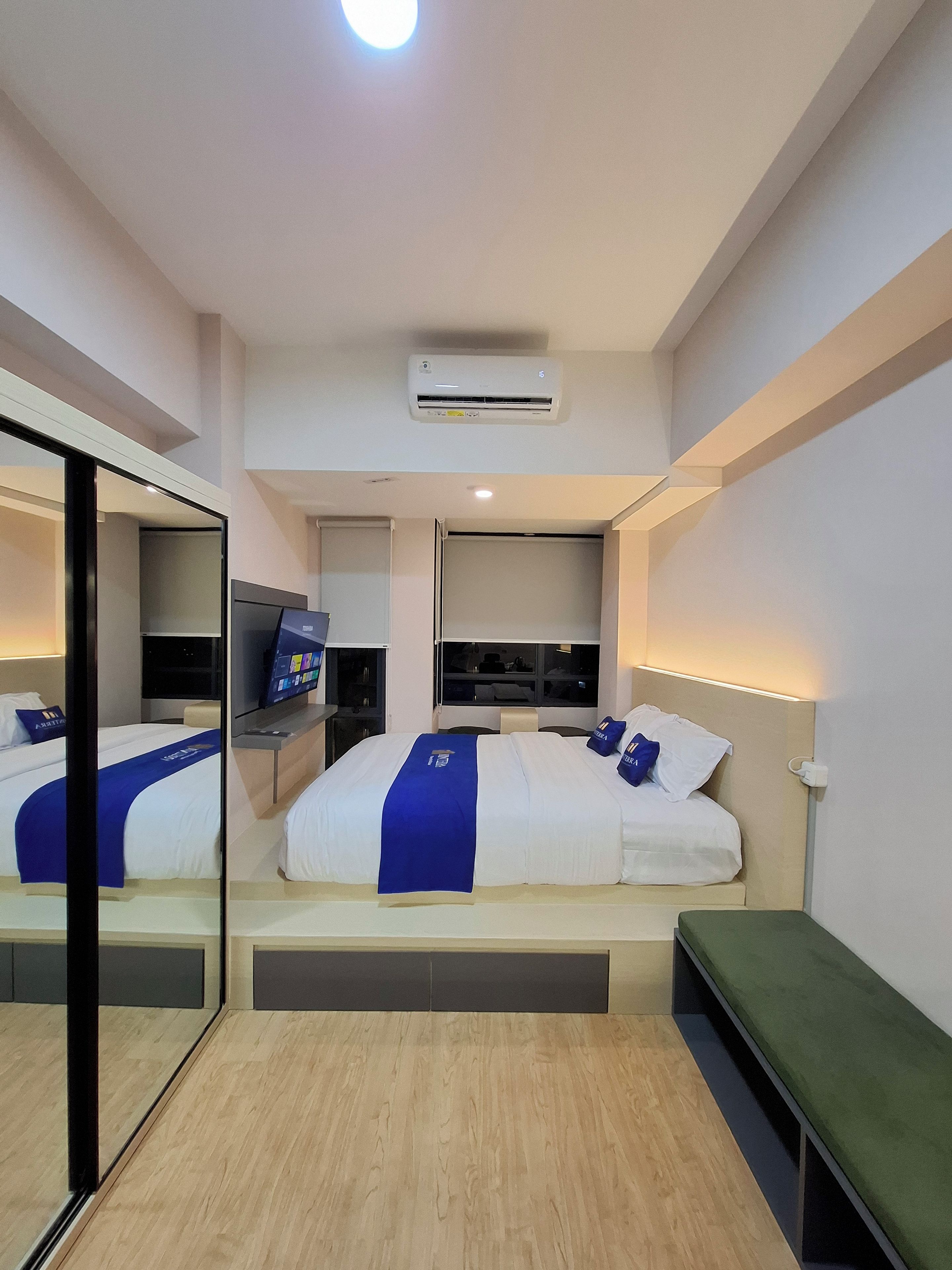 Habitación de hotel moderna con una cama grande, un televisor, un aire acondicionado y un espejo.