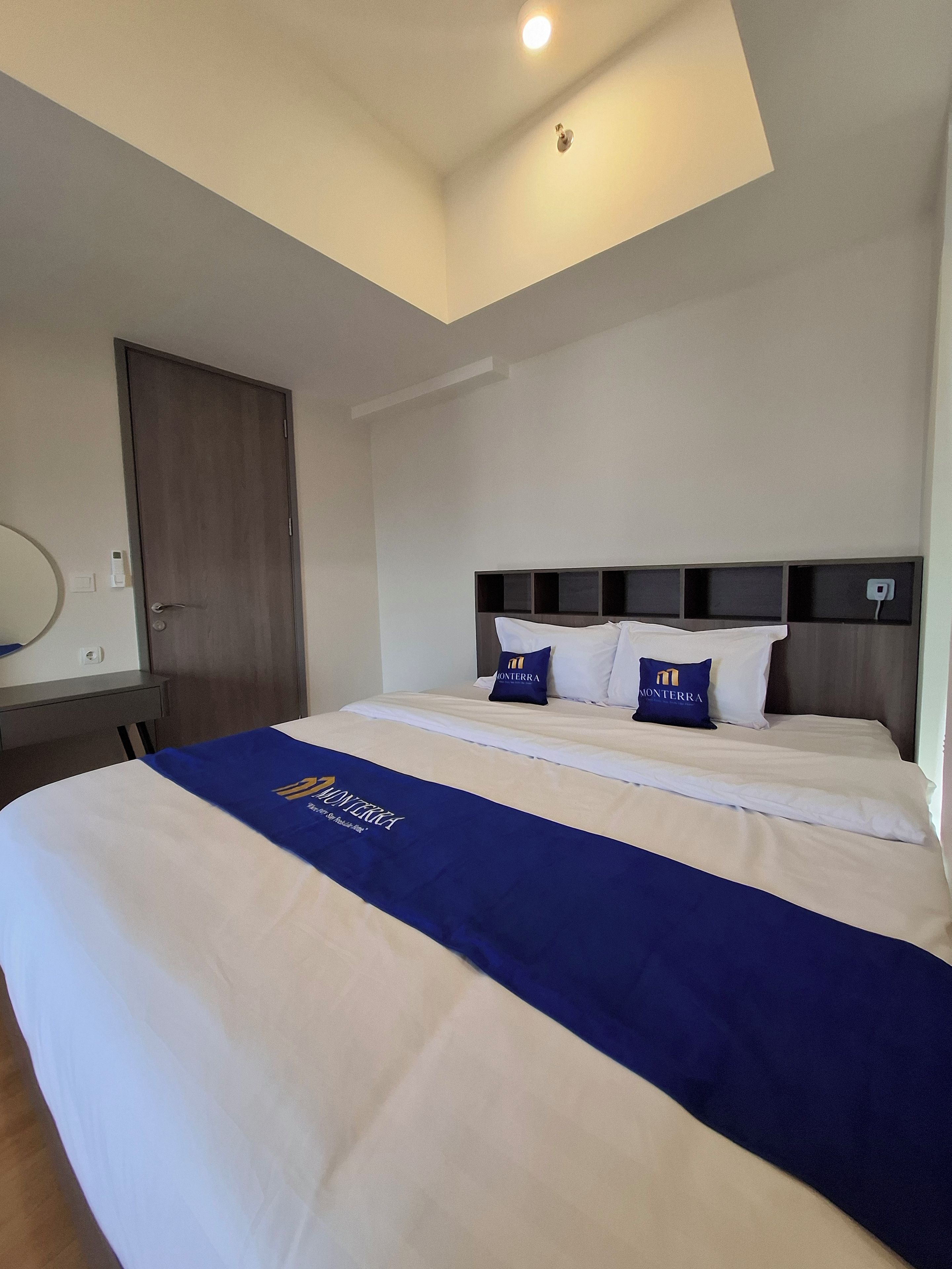 Une chambre d’hôtel avec un lit, un bureau, une chaise, une porte et un luminaire au plafond.