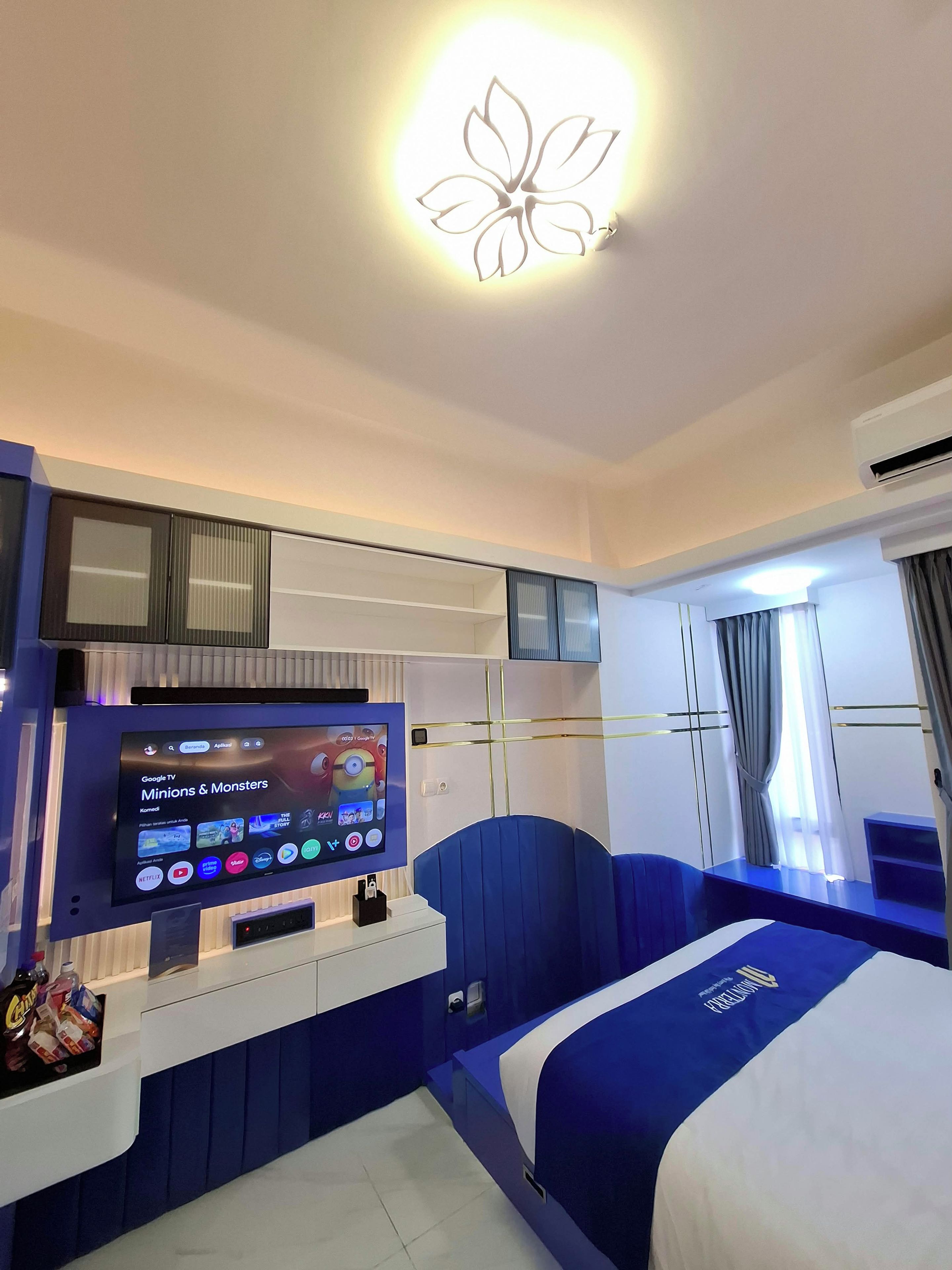 A hotel room with a bed, a TV, a desk, and a wall-mounted light fixture.