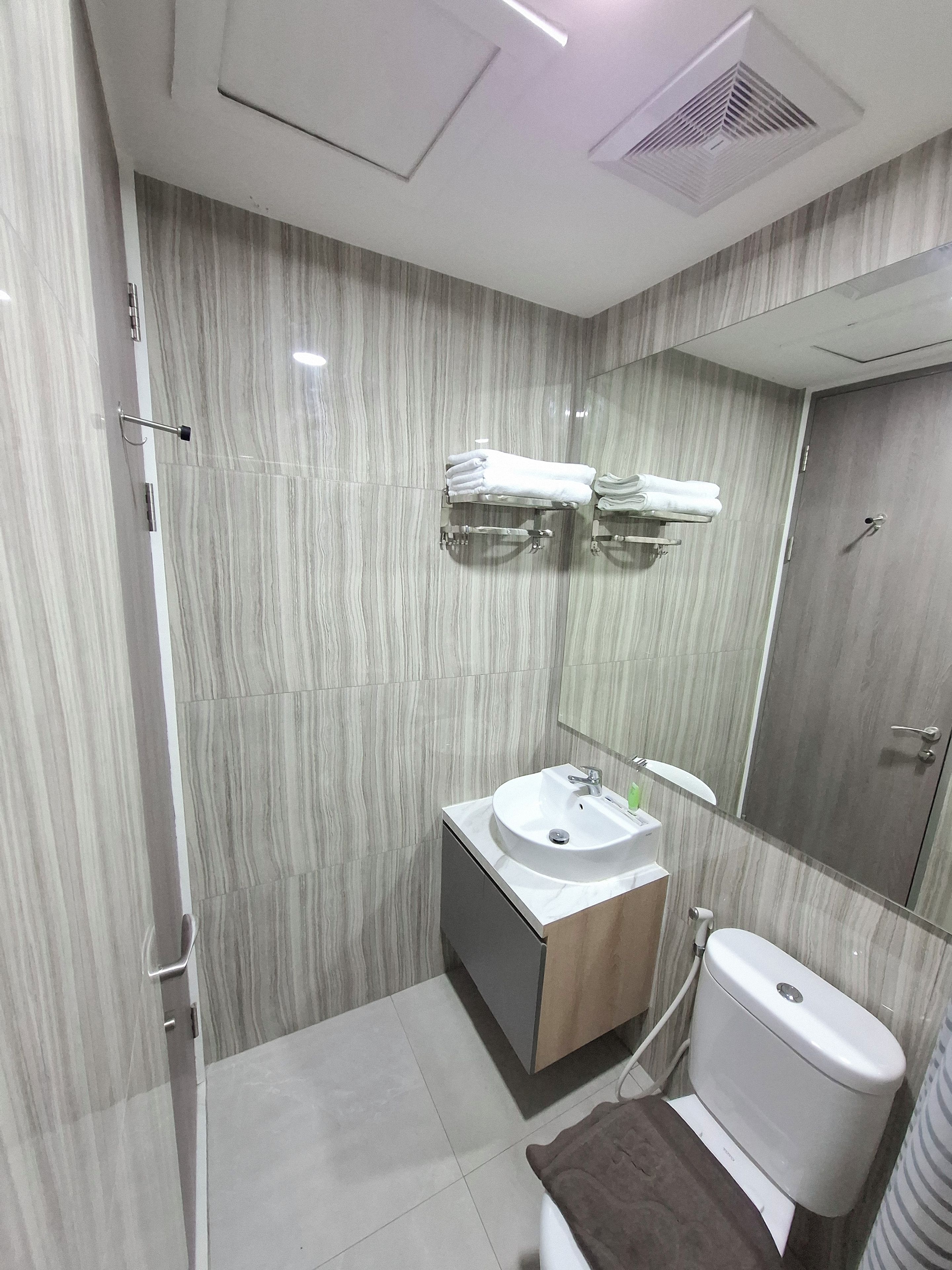 A modern bathroom with a marble wall, a sink, a toilet, and a towel rack.