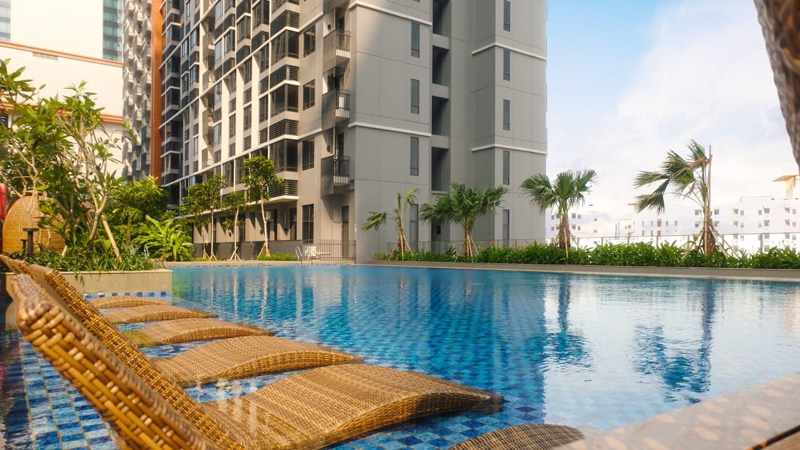 Una piscina con sillas de descanso, rodeada de vegetación y edificios modernos.