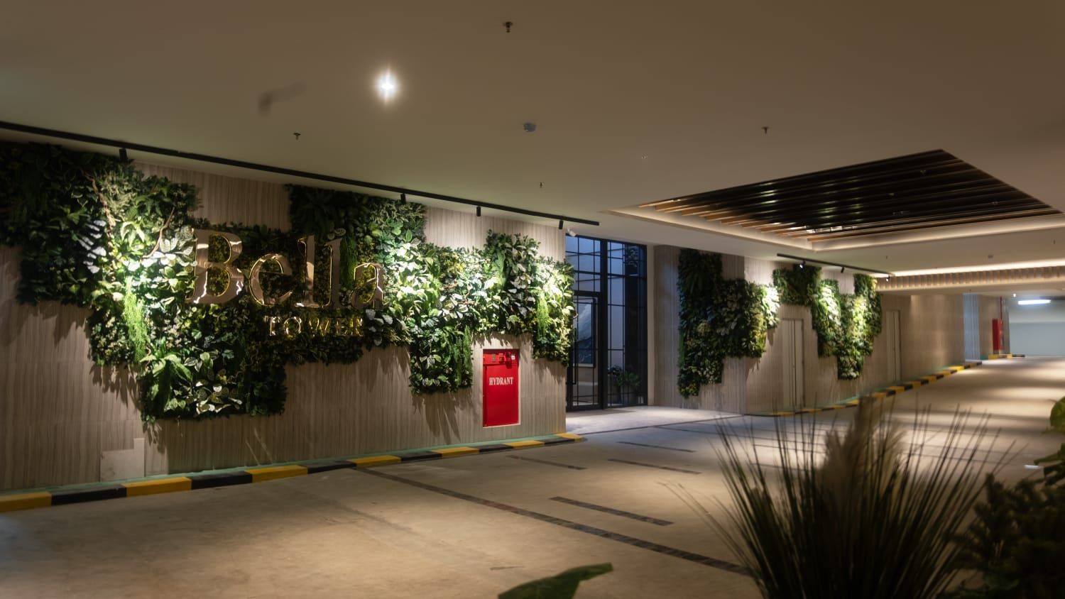 A hallway with vertical gardens, a red hydrant, and a modern ceiling design.