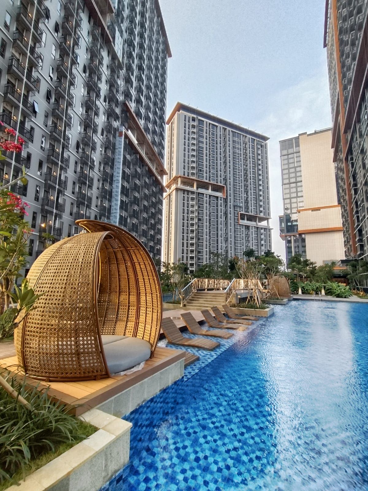 Una piscina con un diseño azul de mosaicos, rodeada por un edificio residencial de gran altura con balcones.
