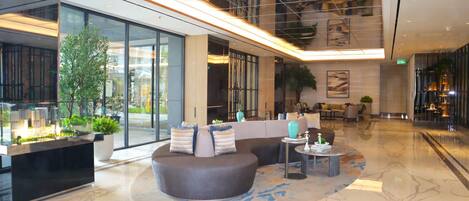 A modern lobby with a reception desk, seating area, and a large window.